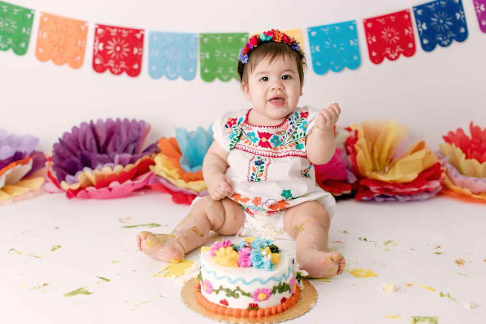 Baby celebrating with cake under colorful papel picado banners and tissue paper flowers.