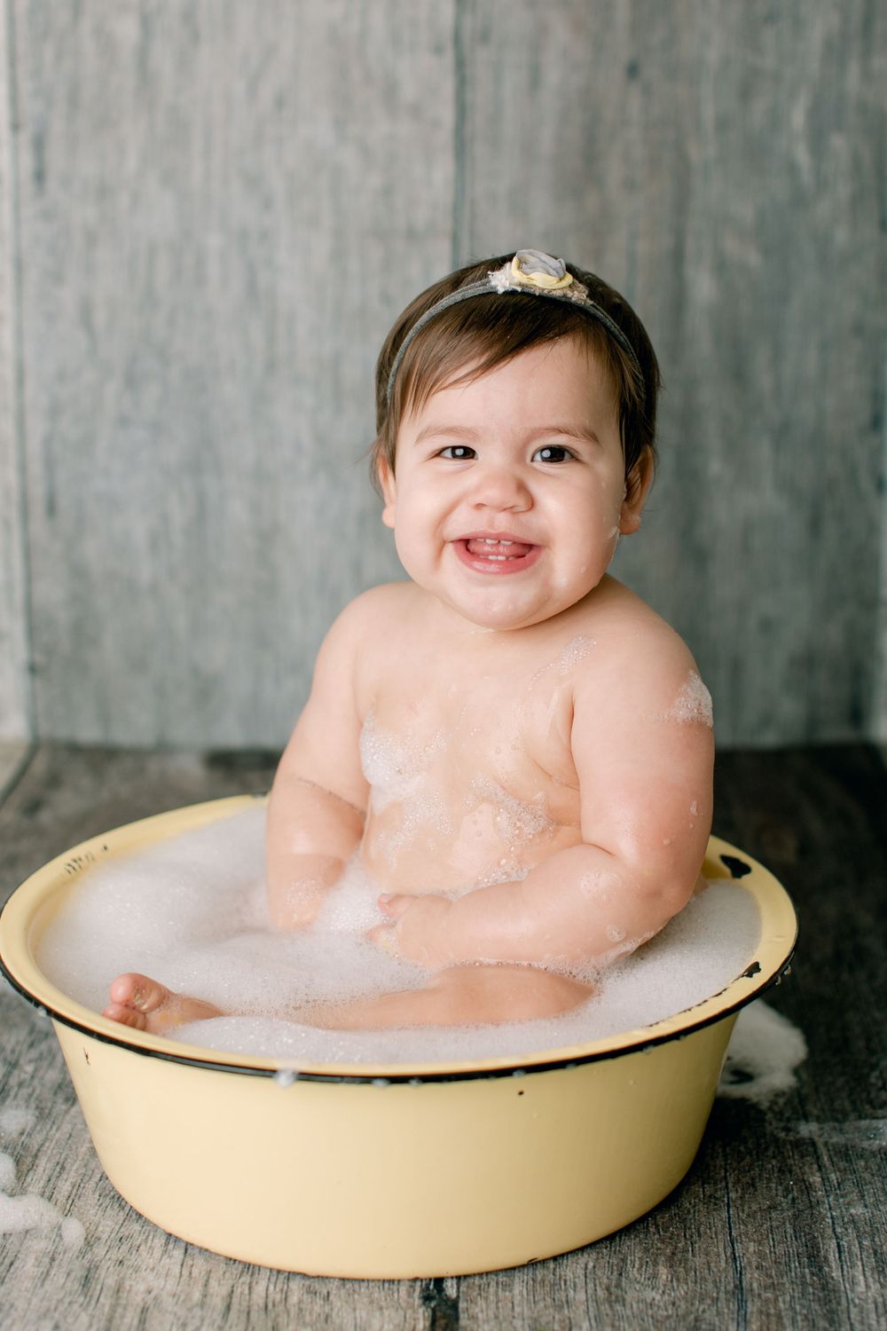 Joyful bath time moment in vintage yellow tub against rustic gray backdrop.