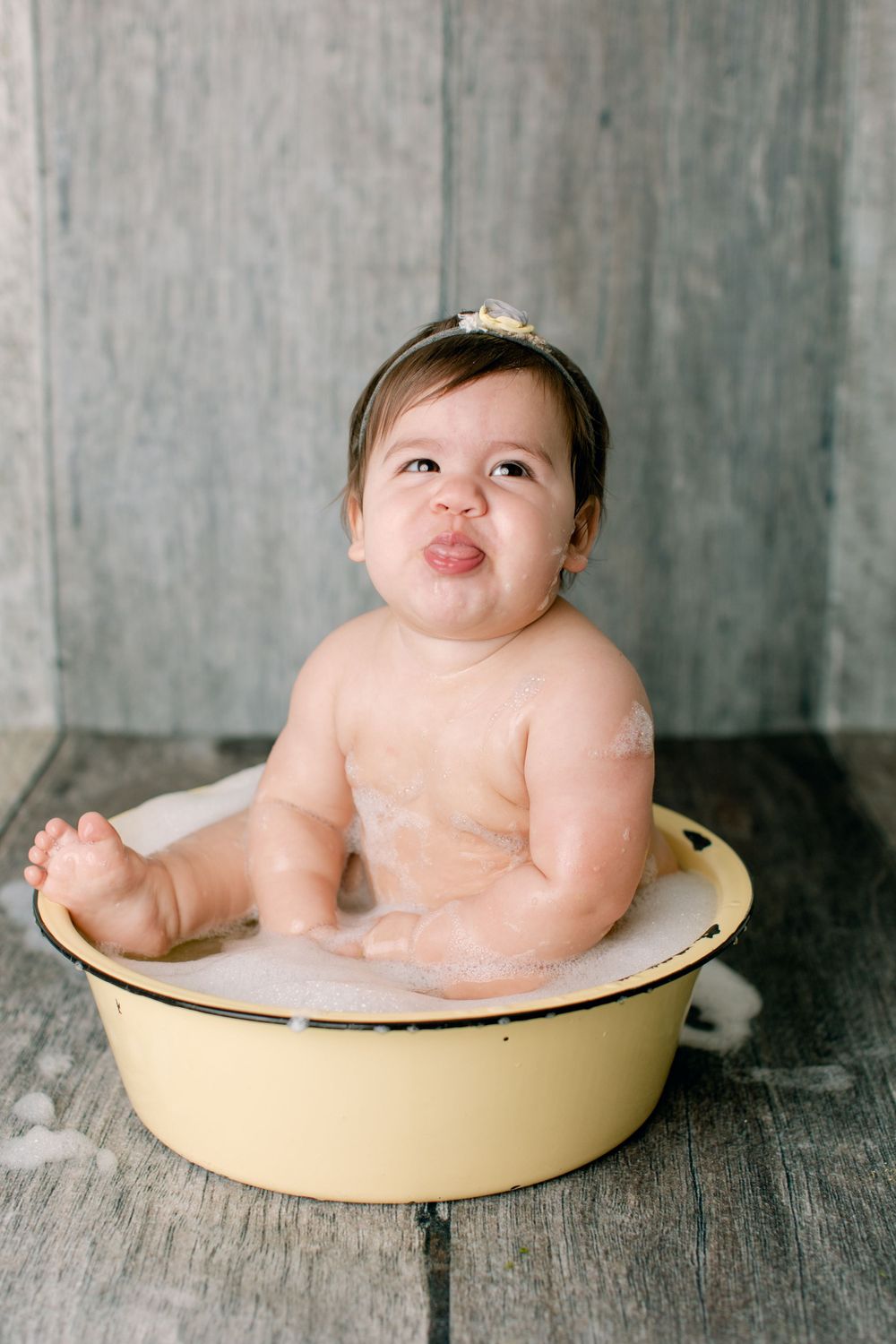 Playful bath time portrait in yellow vintage tub with bubbles and rustic background.