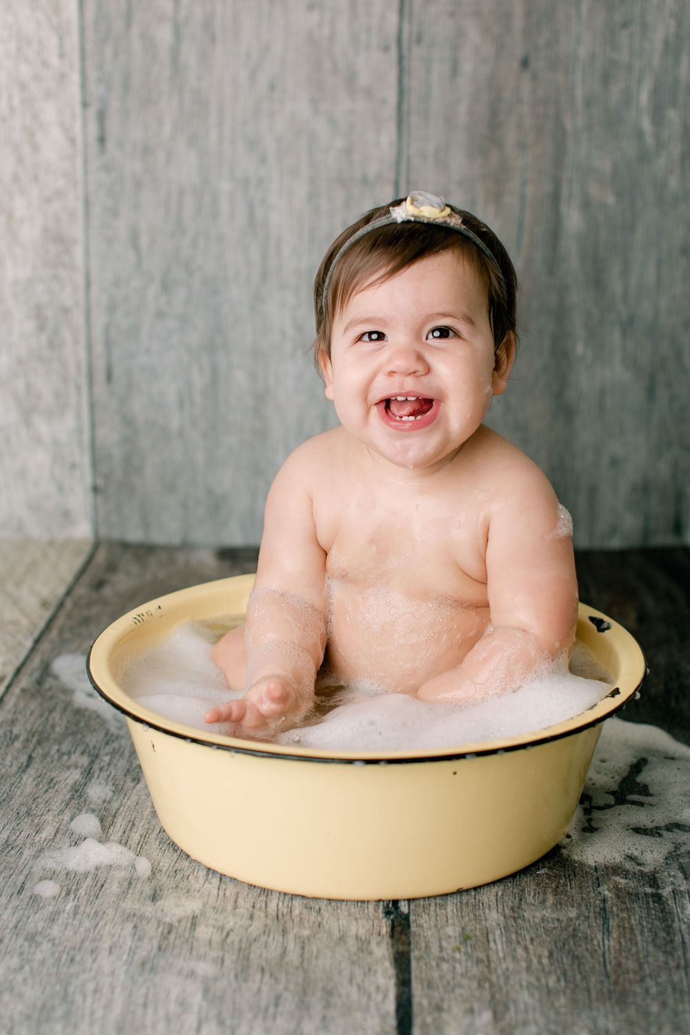 Happy bath time capture in cream-colored vintage tub against weathered wood floor.