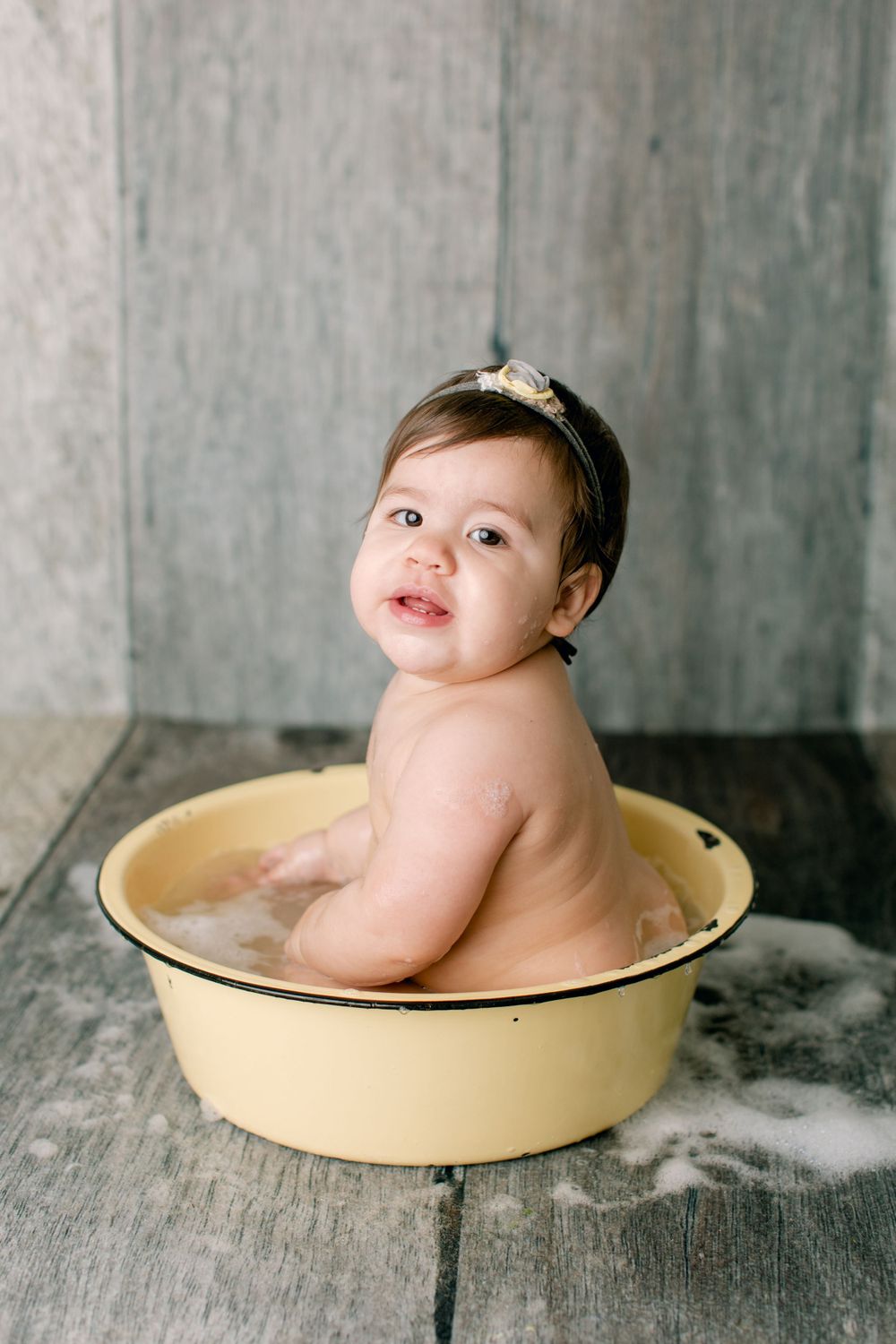 Charming bath portrait in cream-colored vintage tub against gray backdrop.