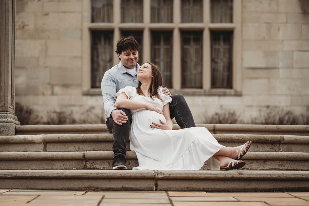 Couple relaxing on stone steps of historic building, pregnant woman leaning against partner.
