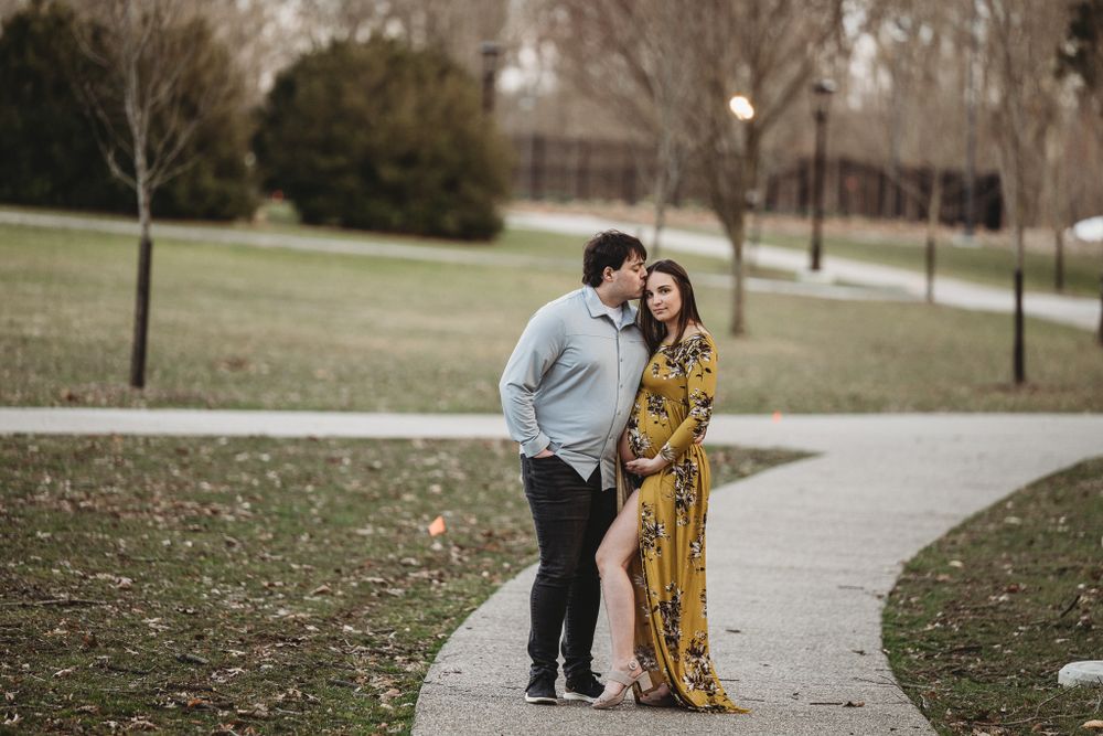 Couple embracing on park pathway, pregnant woman in floral maxi dress with partner.