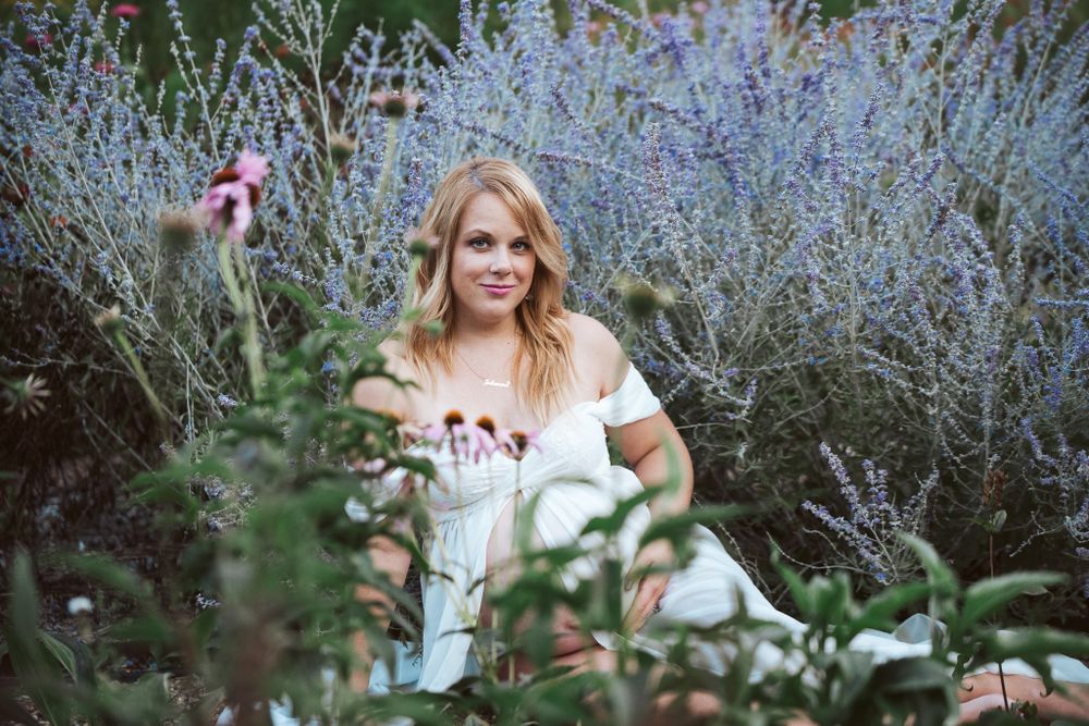 Woman in white dress sitting among lavender and wildflowers in a lush garden setting.