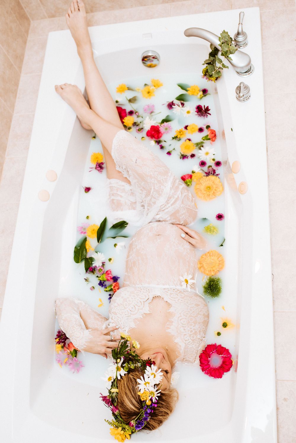Overhead view of pregnant woman relaxing in floral milk bath wearing lace robe.