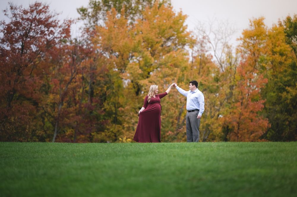 Couple dancing on green lawn with vibrant fall foliage trees in background.