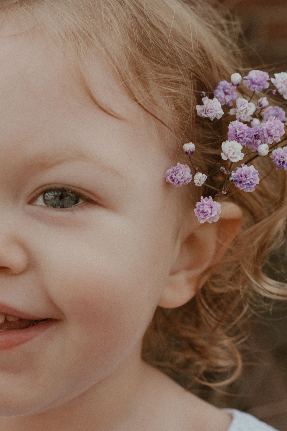 Delicate purple flowers adorn blonde curls in this ethereal close-up portrait.