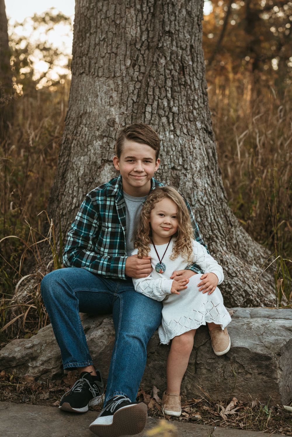 Siblings share a sweet moment sitting together on large tree roots in autumn.