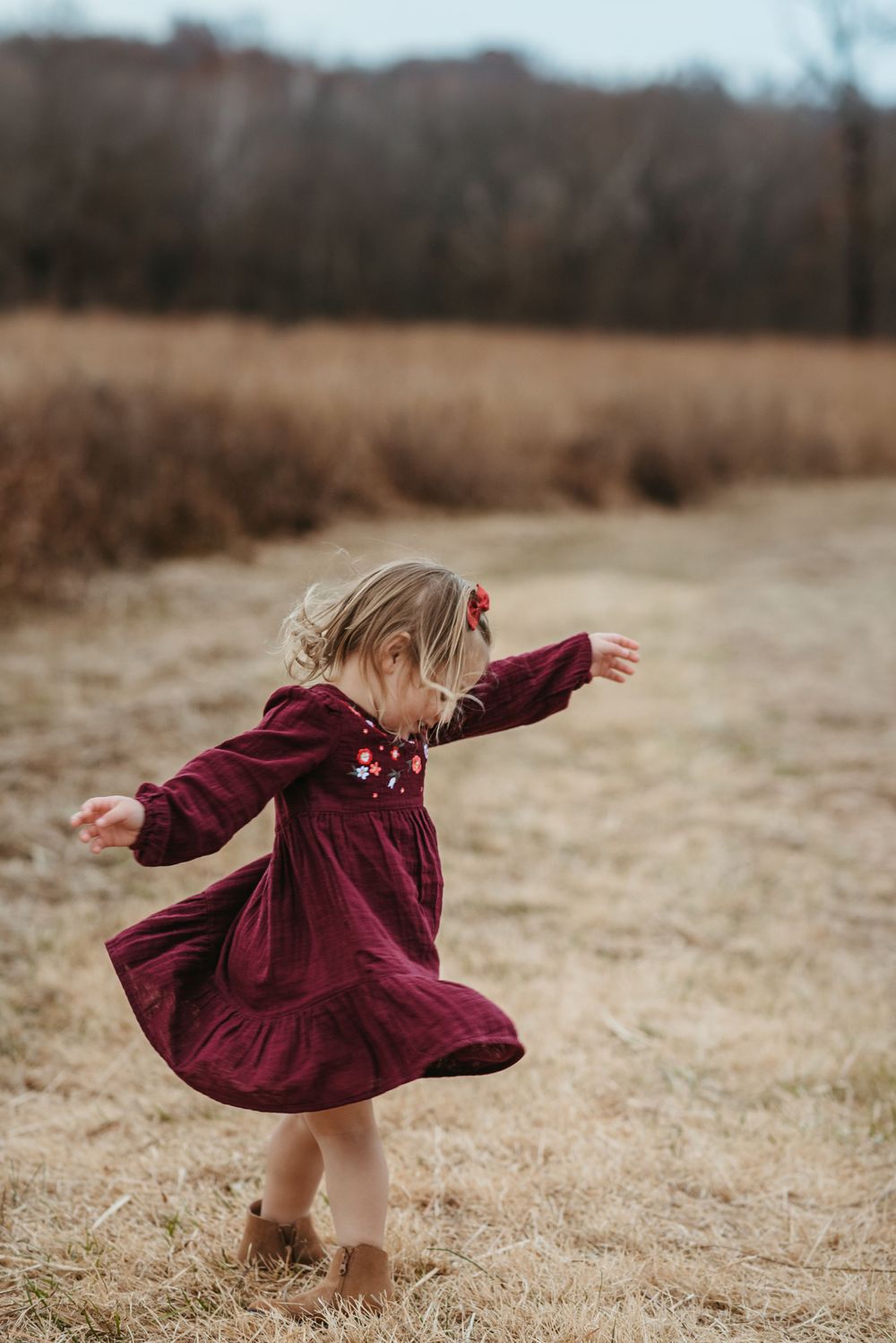 Child in burgundy dress twirling and dancing in autumn field.
