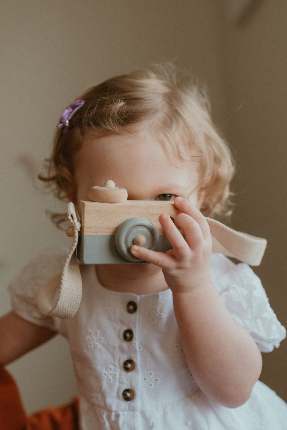 A dreamy vintage scene of someone playing with a wooden toy camera in a white eyelet dress.