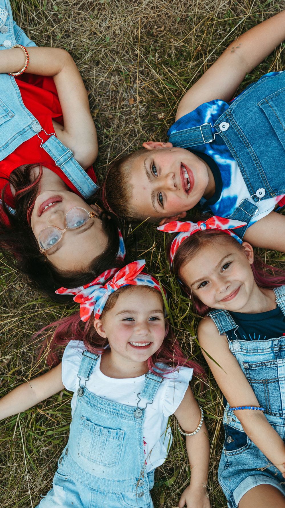 Children lying in grass wearing denim overalls and red bandanas.