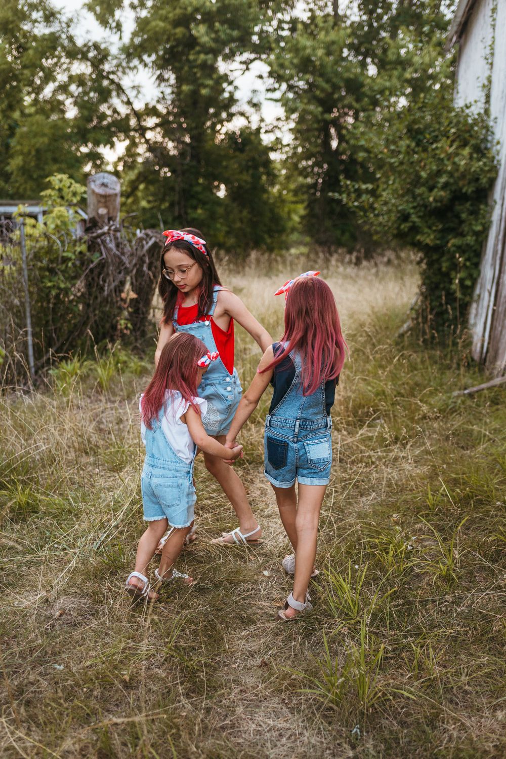Children playing and exploring in tall grass near an old rustic building.