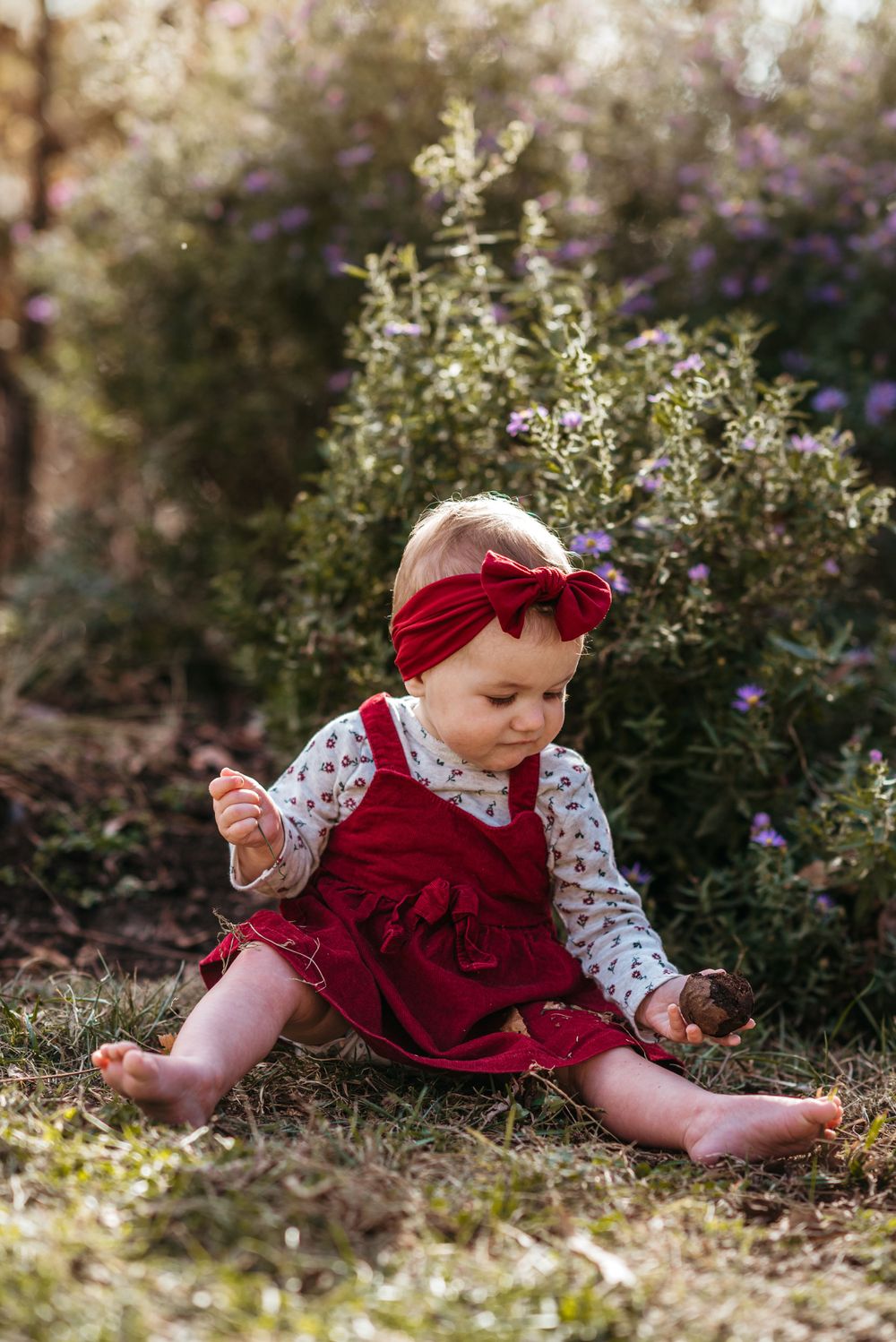 Baby in red dress crawling through garden with purple flowers blooming.
