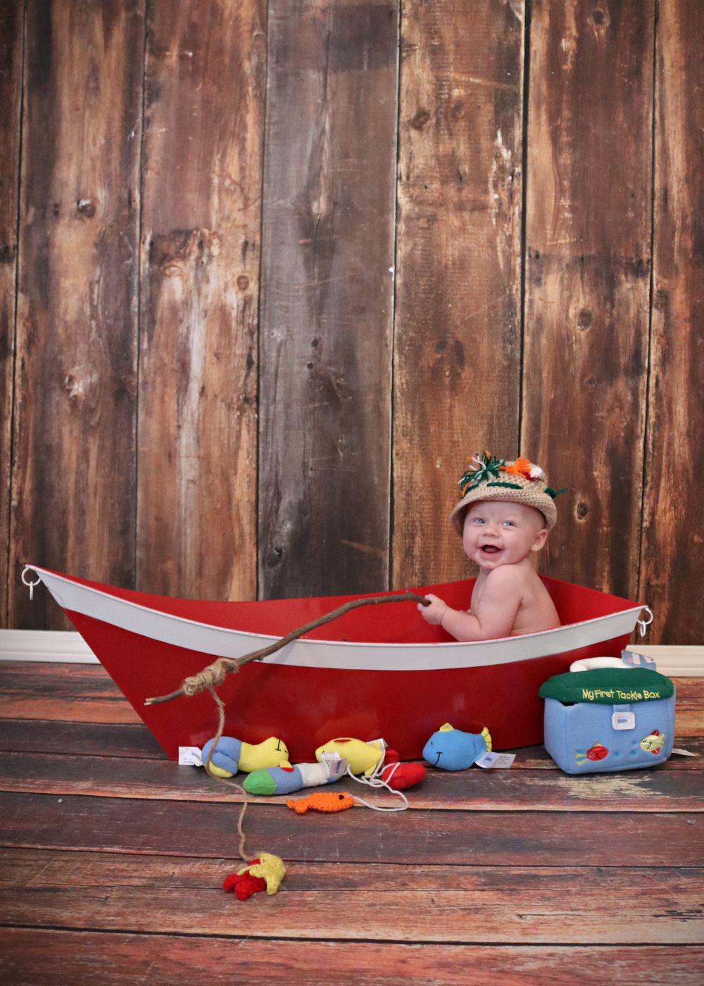 Bath time setup with red boat tub and colorful toy fish on wooden floor.