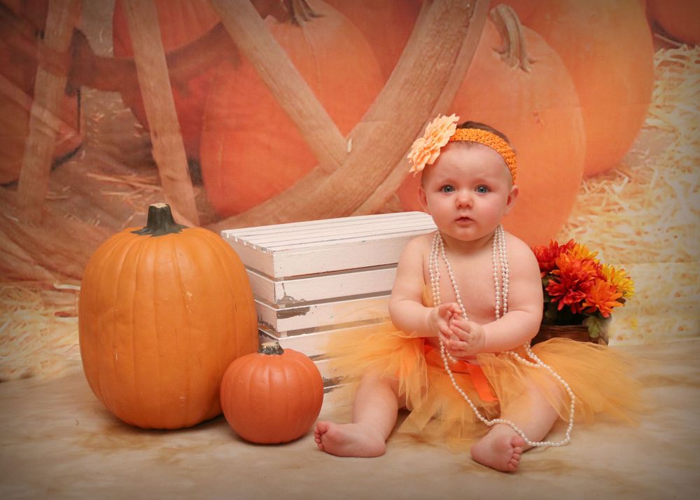 A festive fall photo setup with pumpkins, wooden crates, and an orange tutu against an autumn-colored backdrop.