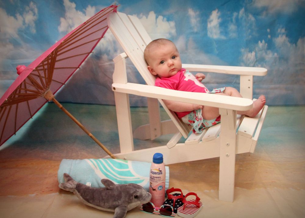 A beach scene setup with a white chair, red parasol, and summer accessories.