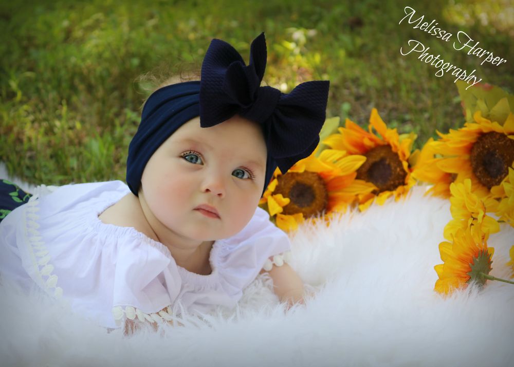 Portrait with navy bow headband and sunflowers on white fur backdrop.