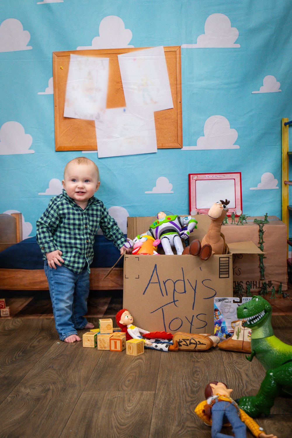 Toy Story themed photo setup with cloud backdrop and collection of toys on wooden floor.