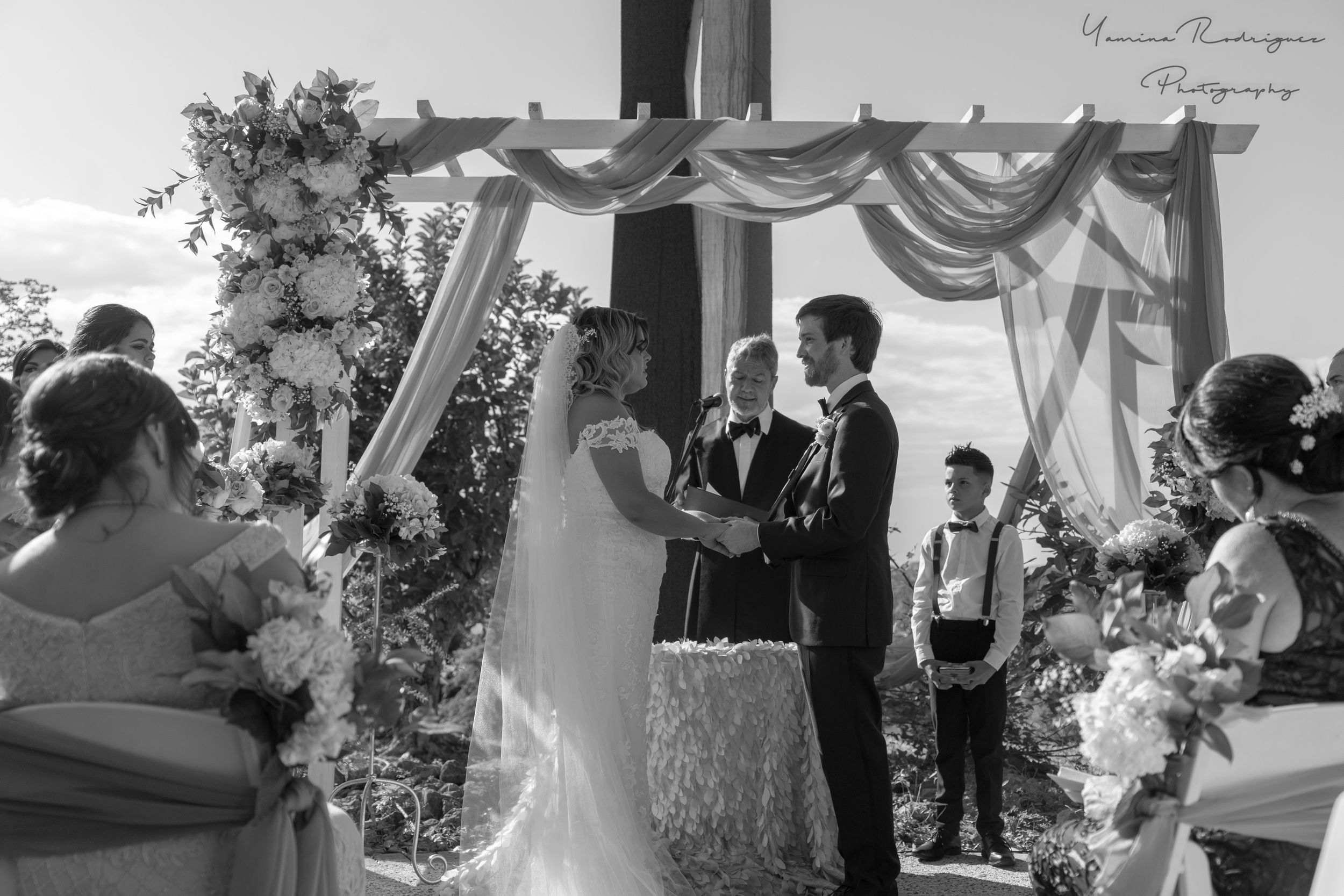 Black and white wedding ceremony photo under draped arch with floral decorations.