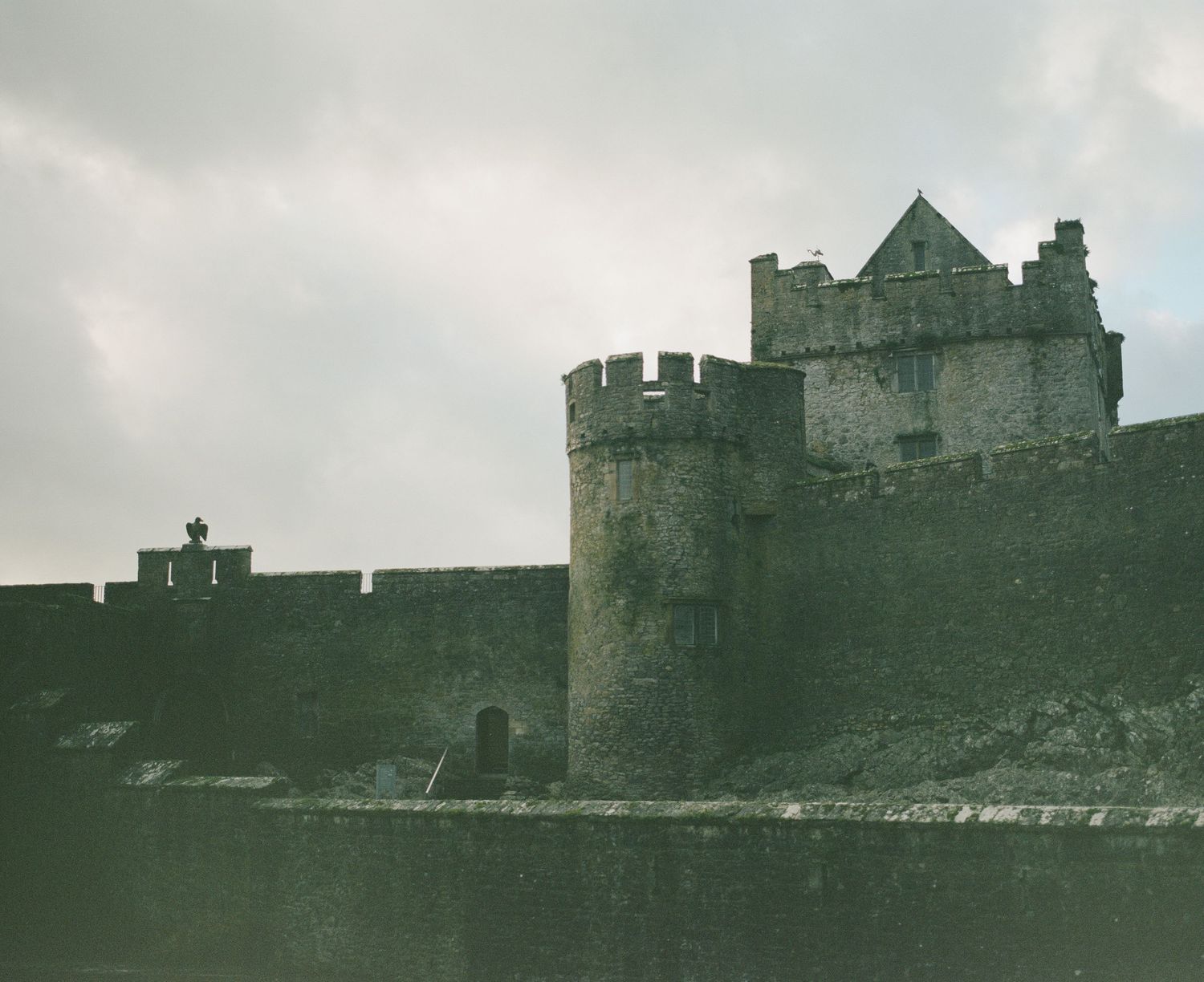 Medieval castle with tall towers and battlements perched on a rocky shoreline under cloudy skies.