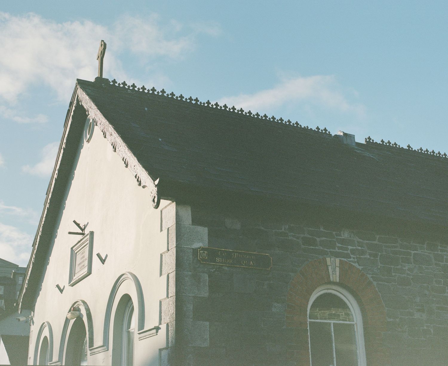 White church building with arched windows and decorative roof trim against a cloudy sky.