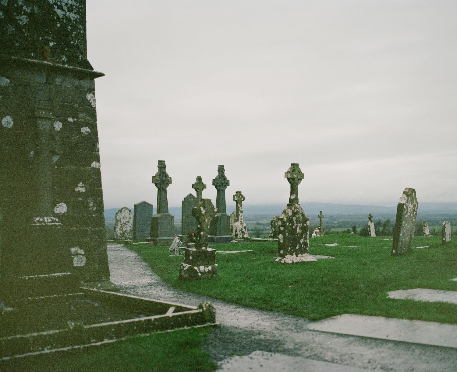 Celtic crosses and gravestones in a historic church cemetery with mountains in background.