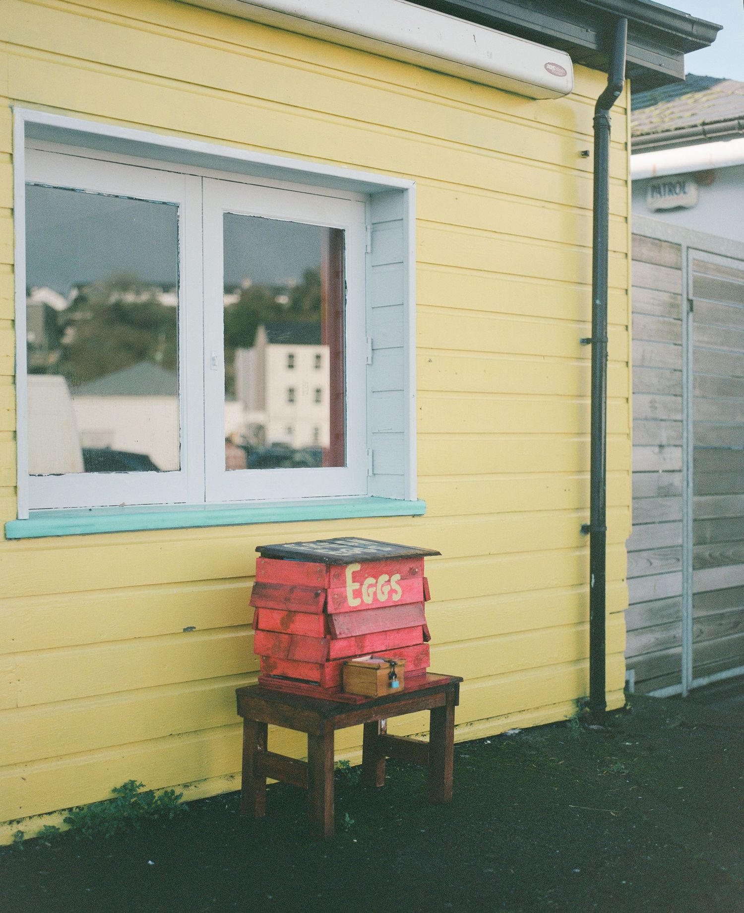 Yellow cottage with white trim and a red wooden box on a small bench outside the window.