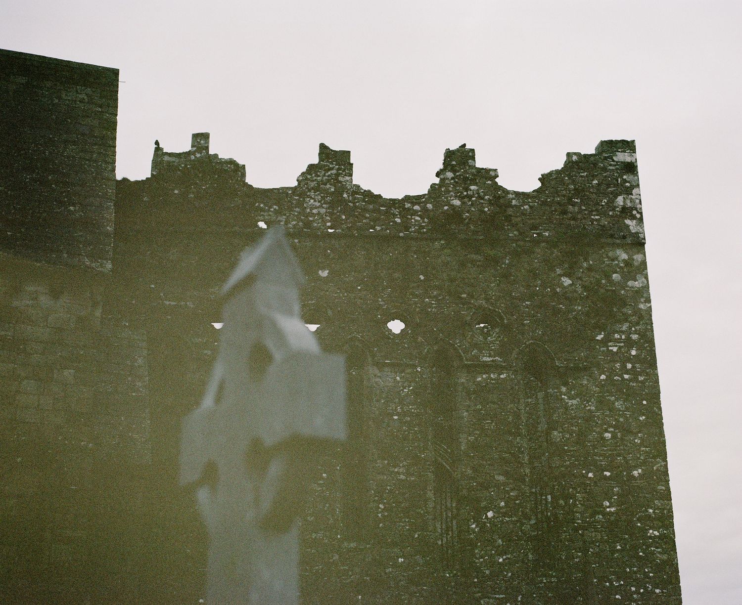 Silhouette of a Celtic cross against ancient stone castle walls.