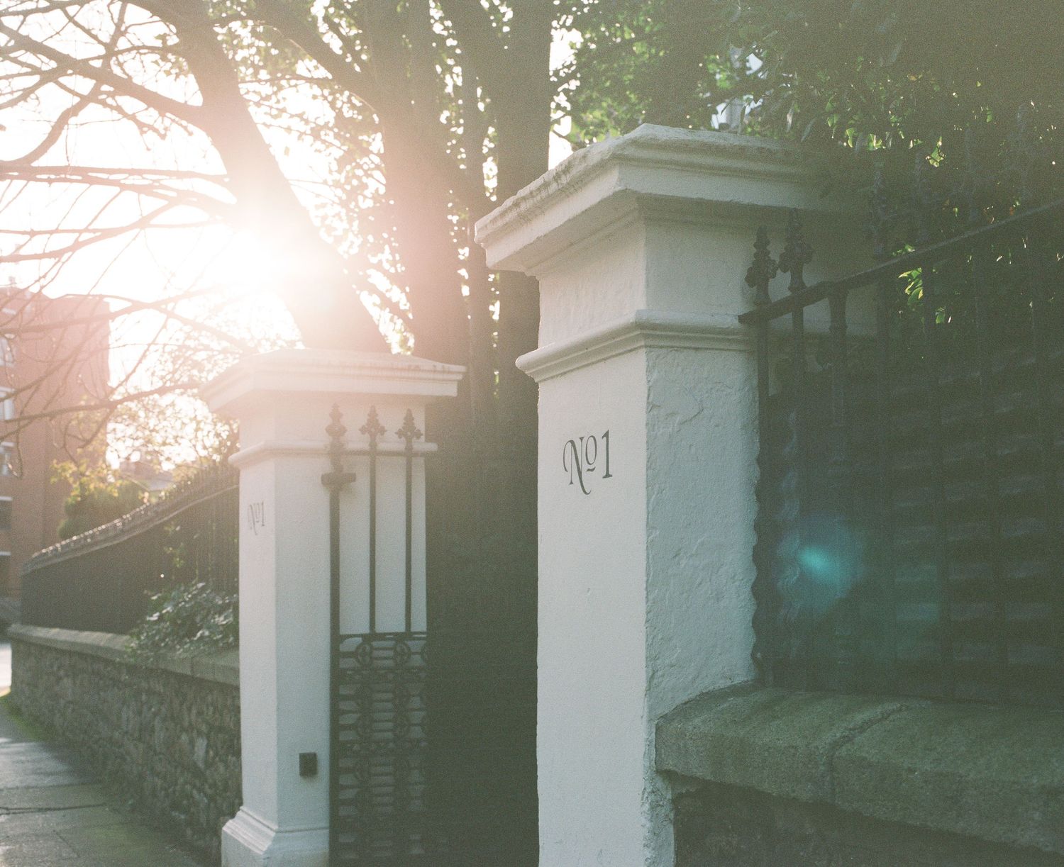 White stone entrance pillars with wrought iron details captured during golden hour with sun flare.