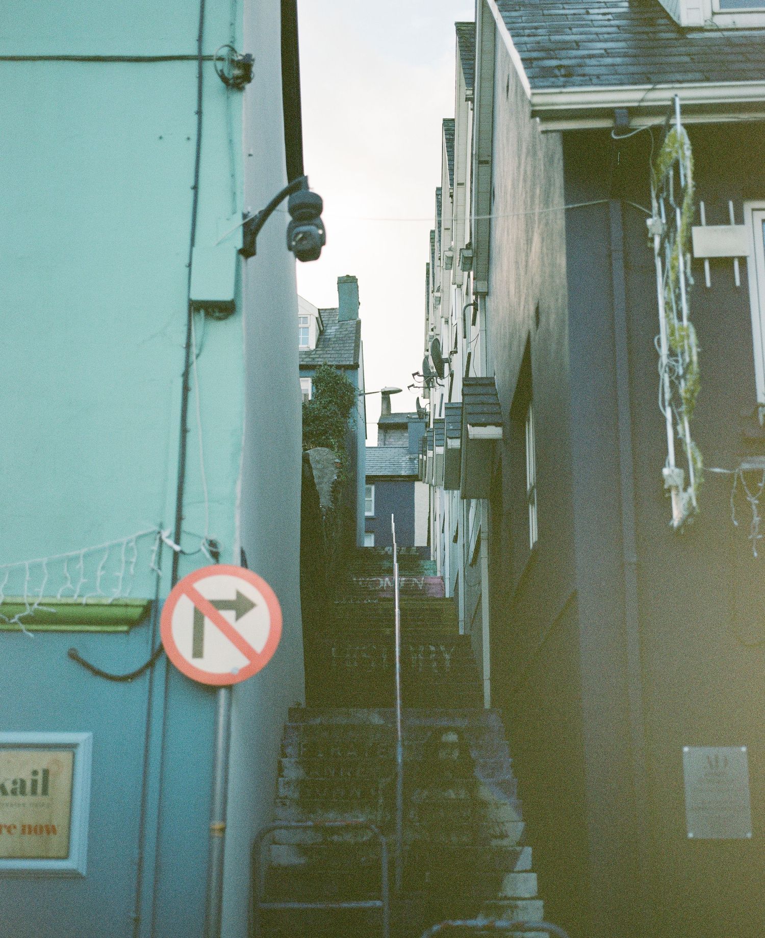 Narrow alley between turquoise buildings with a no parking sign and steep steps in the distance.