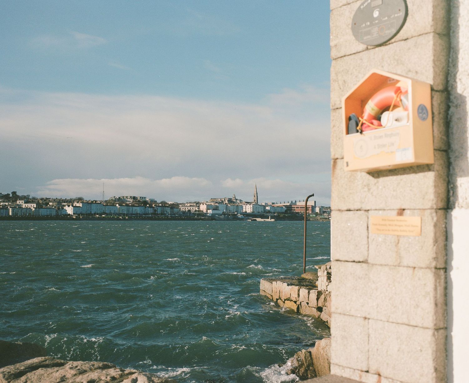 Coastal view of a harbor with industrial ships and an orange building detail in the foreground.