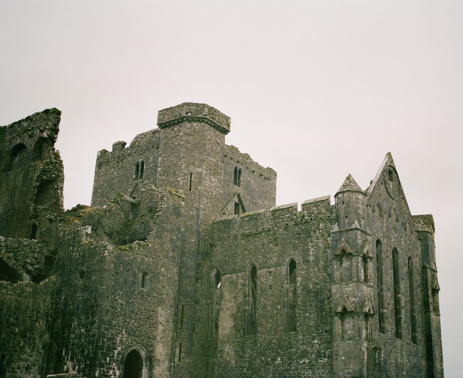 Medieval stone castle ruins with Gothic architectural features against cloudy sky.