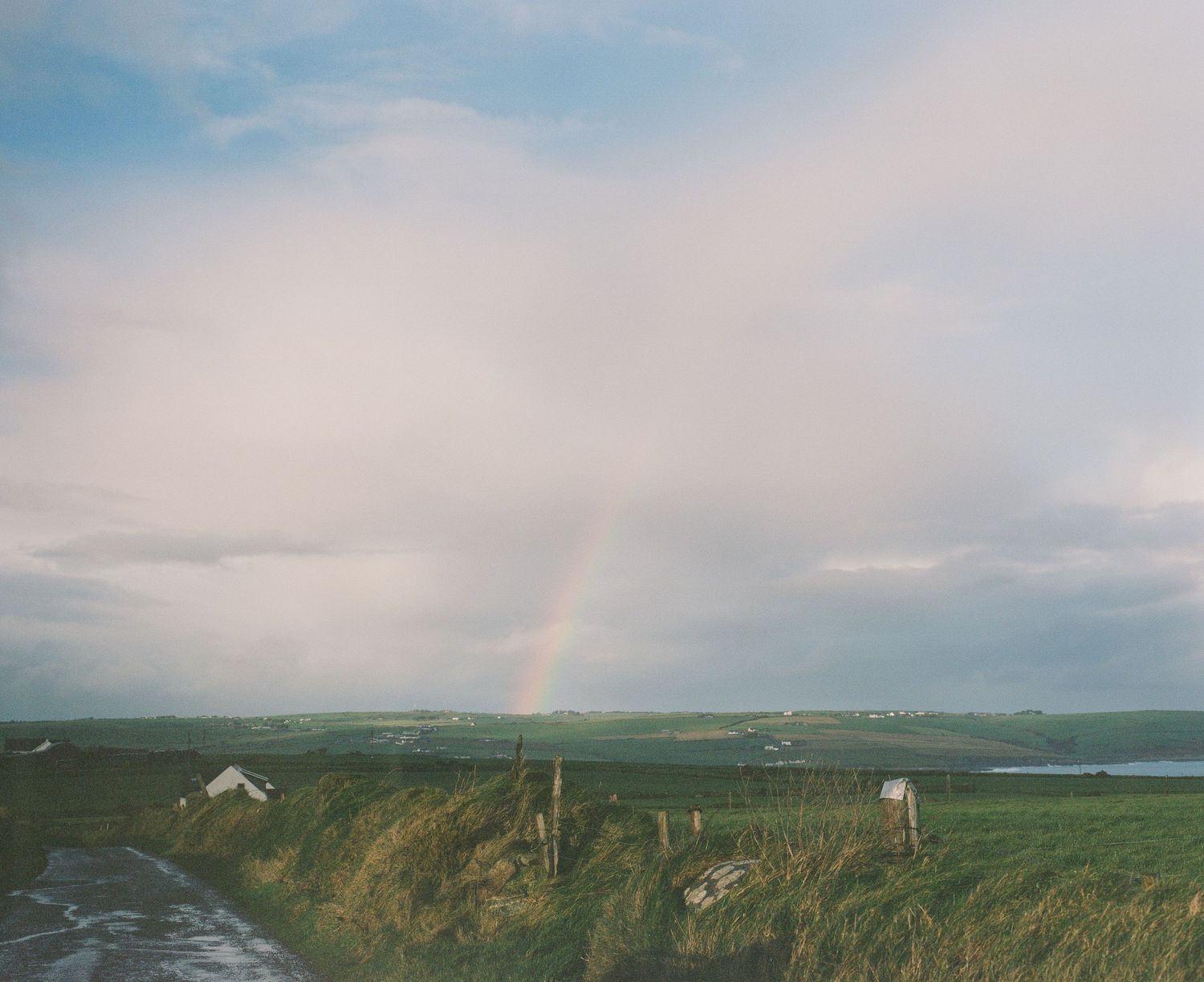 Rainbow appears over green coastal fields and distant ocean views.