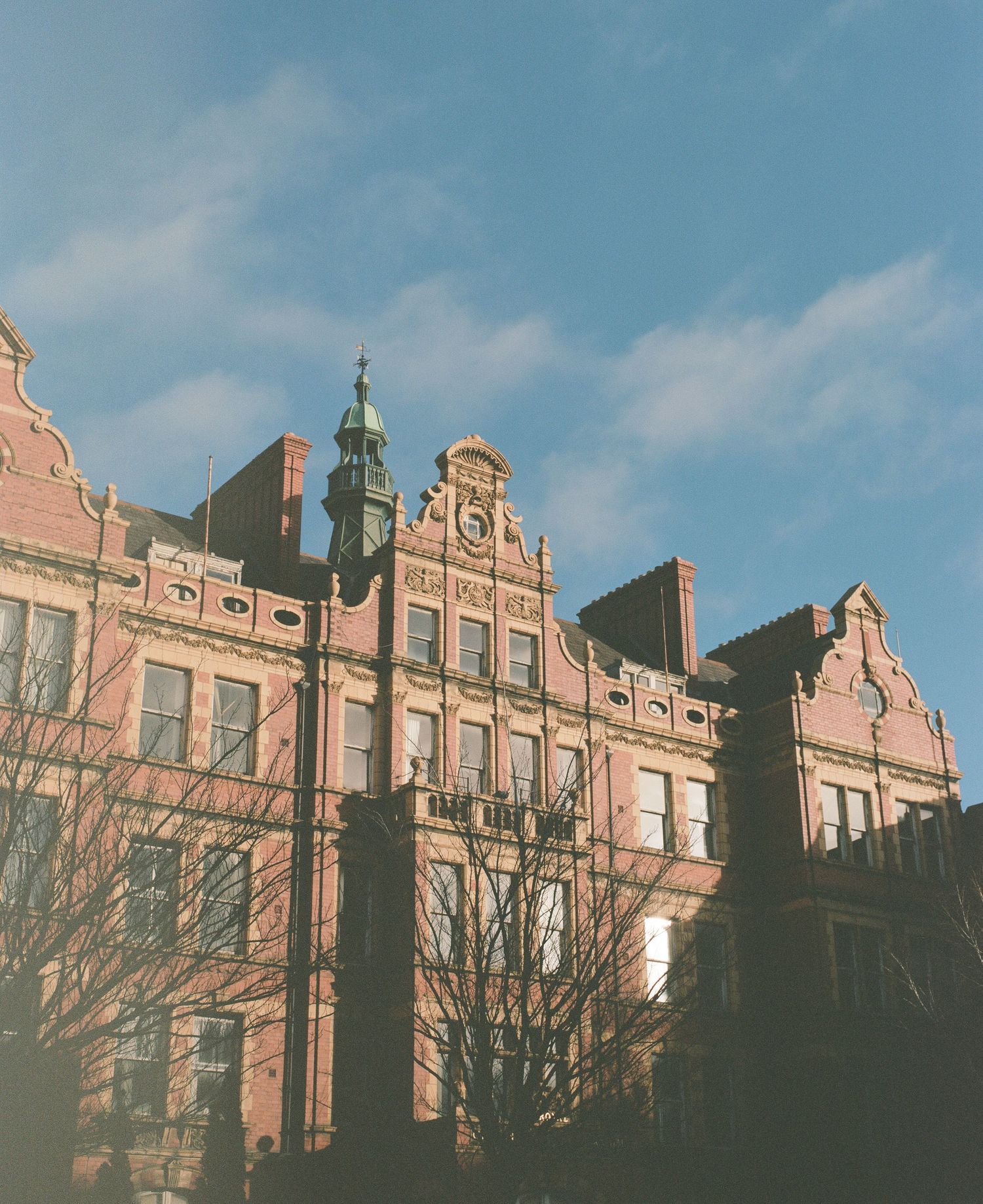 Ornate red brick Victorian building with decorative stonework and multiple windows against blue sky.