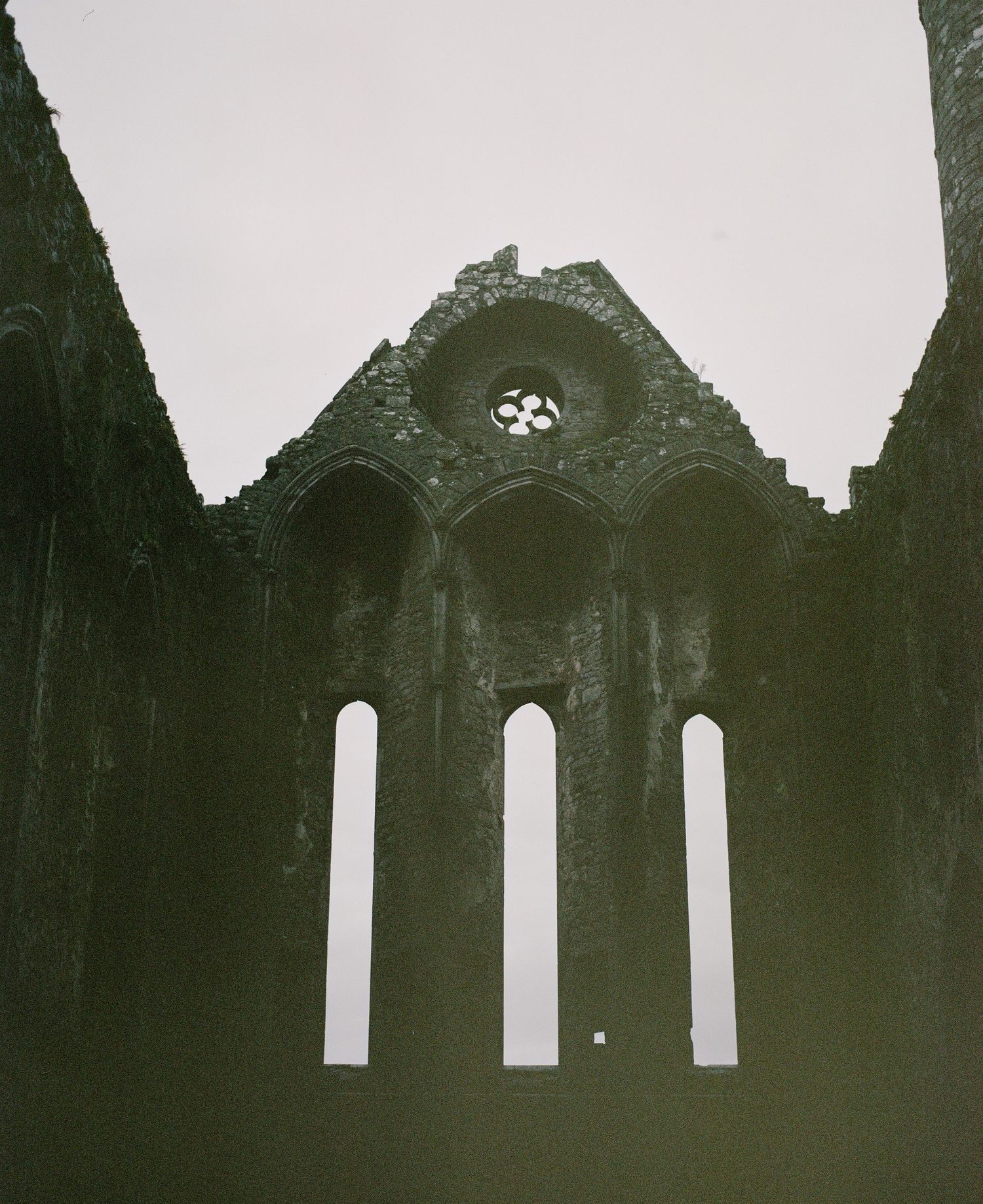 Three Gothic arched windows in a ruined church wall with ornate stone tracery.