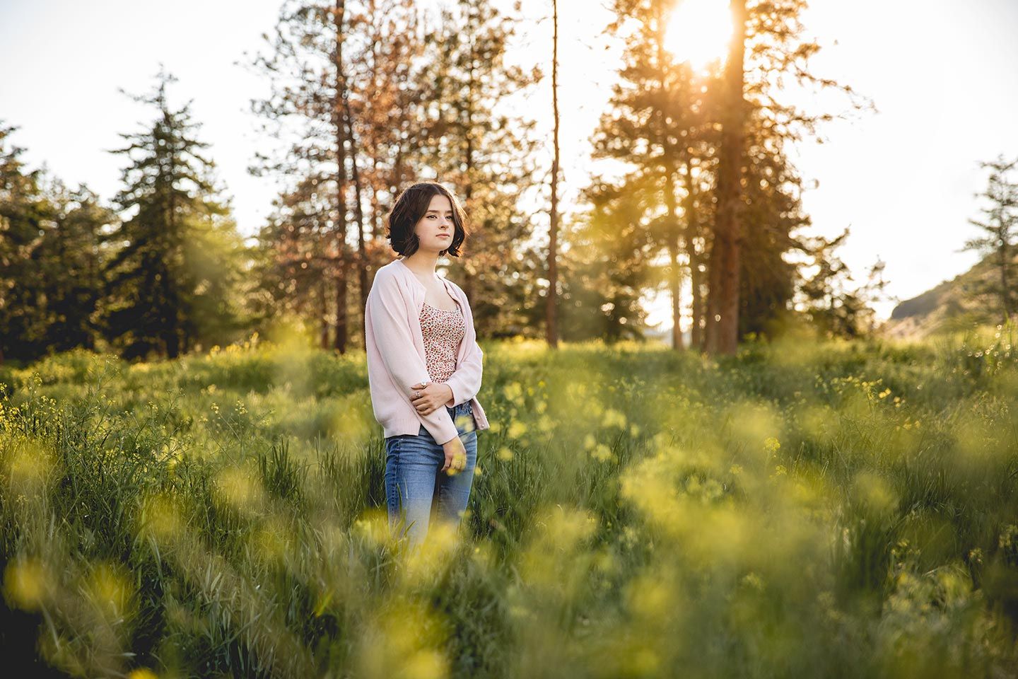 high school senior girl stands in the mountian wildflowers with the sun setting