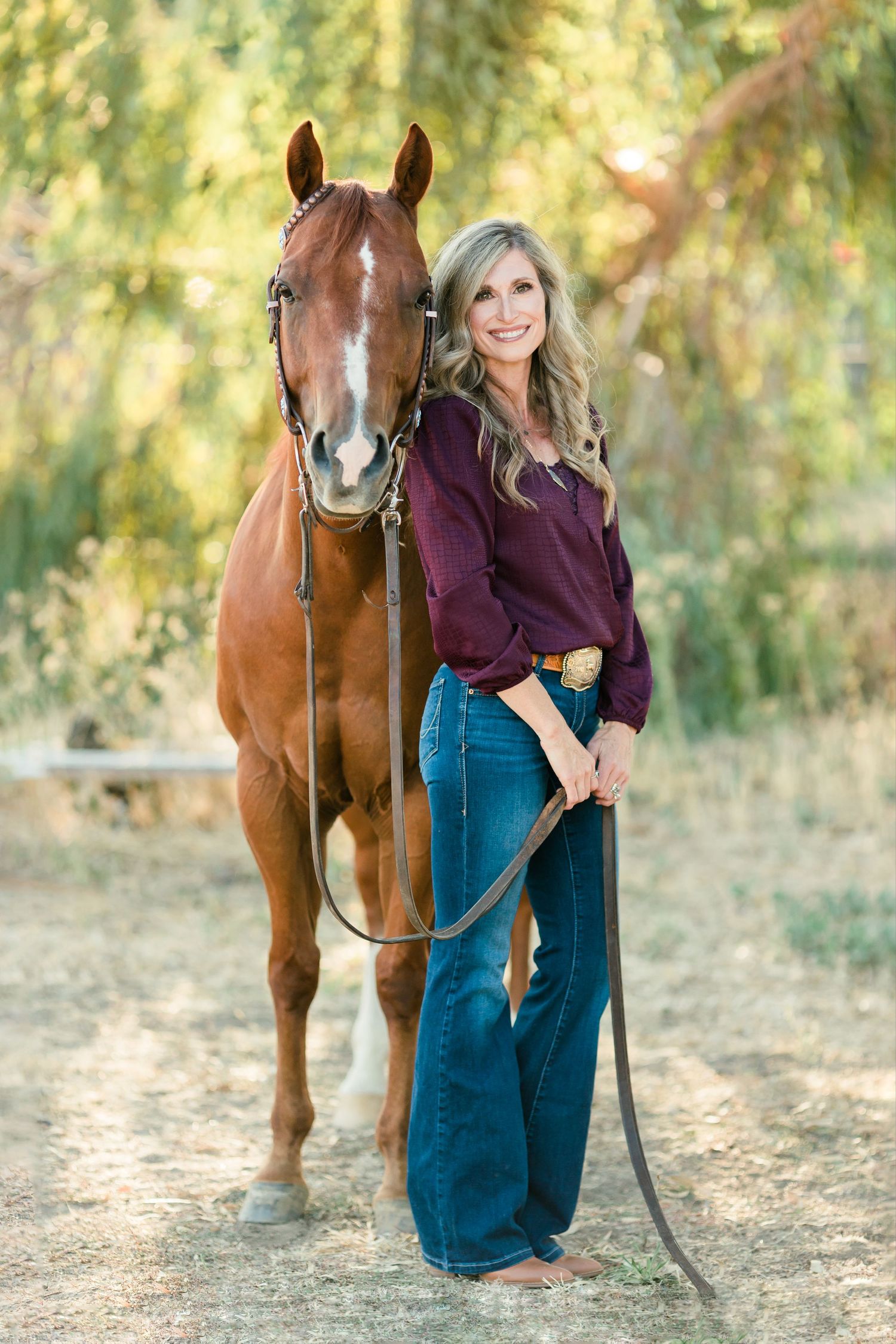 Woman in purple sweater poses with beautiful brown horse in autumn setting.