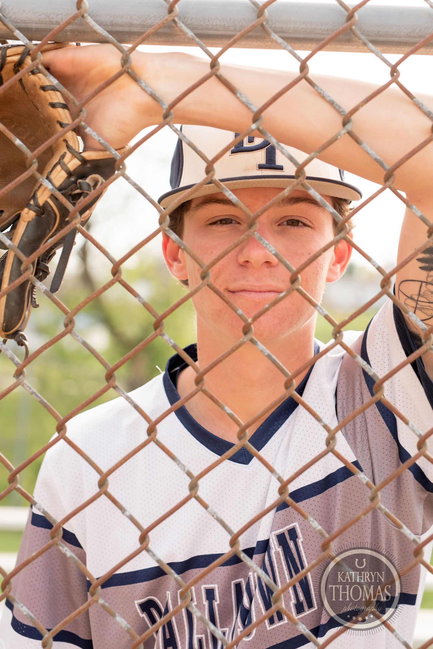 Baseball player seen through chain-link fence wearing Dellasoft uniform and cap.