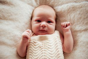 Smiling newborn baby in cream knitted sweater rests on white blanket.
Altona Family Photographer Melbourne