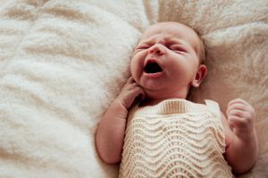 Newborn baby wearing cream knit sweater yawns while lying on white bedding.
Altona Family Photographer Melbourne