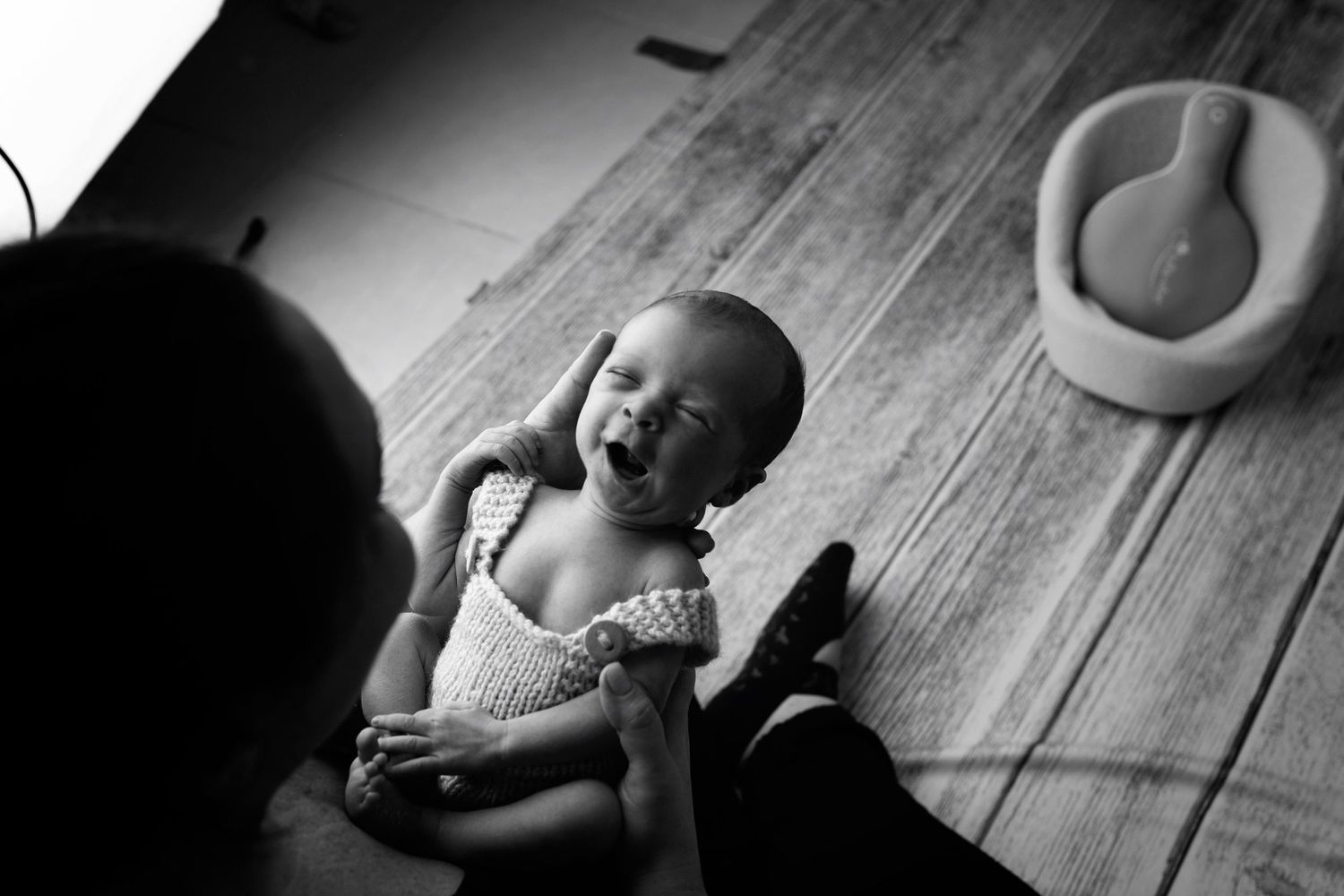 Black and white photo of a small baby smiling while lying on a wooden floor.