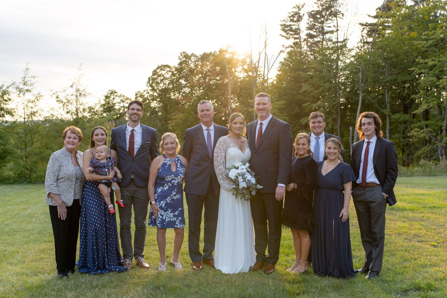 Wedding party group photo at sunset with trees in background.