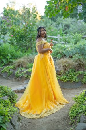 Person wearing flowing yellow gown poses in lush garden setting.