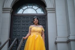 Person in yellow ballgown poses on steps in front of grand arched doorway.
