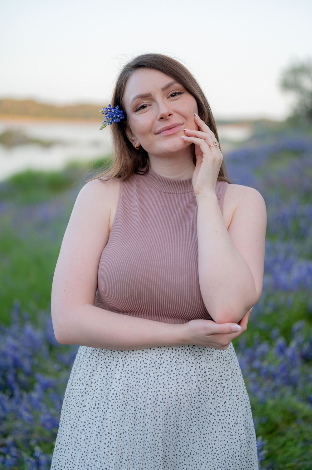 Portrait in a field of bluebonnets wearing a pink turtleneck and floral skirt.