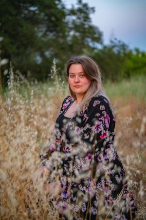Woman in floral dress poses among tall grass and wildflowers.