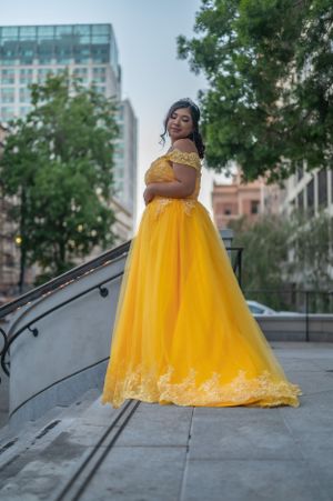 A stunning yellow ballgown with lace trim photographed against an urban backdrop with modern buildings.