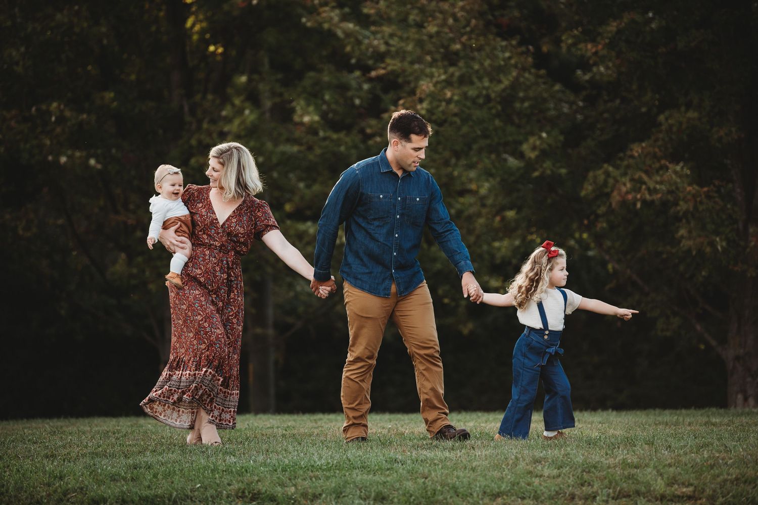 A family walks together on green grass during an outdoor photo session at sunset.