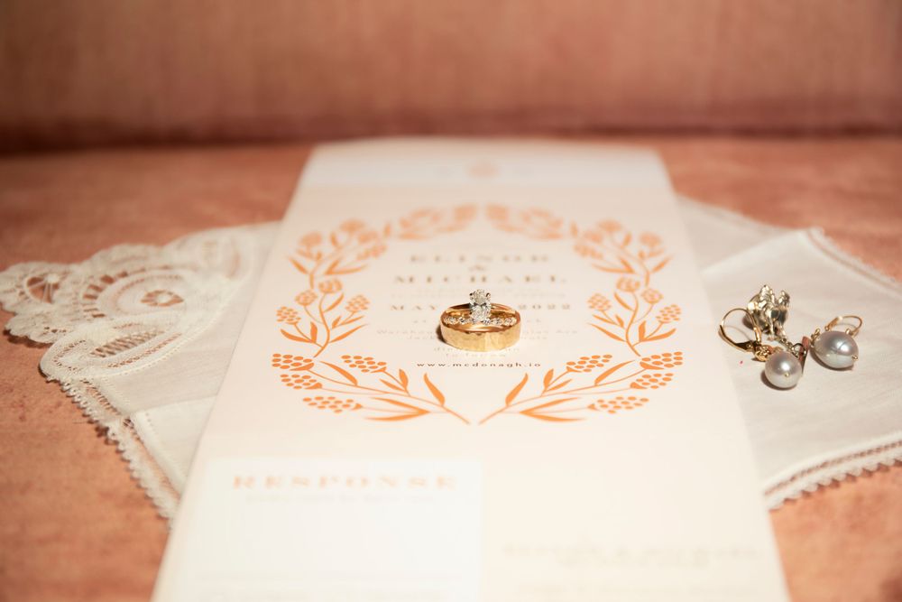 Wedding rings rest on a vintage lace handkerchief with orange floral embroidery detail.