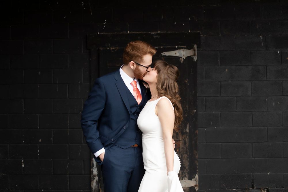 A romantic moment captured between newlyweds against a dark industrial wall.